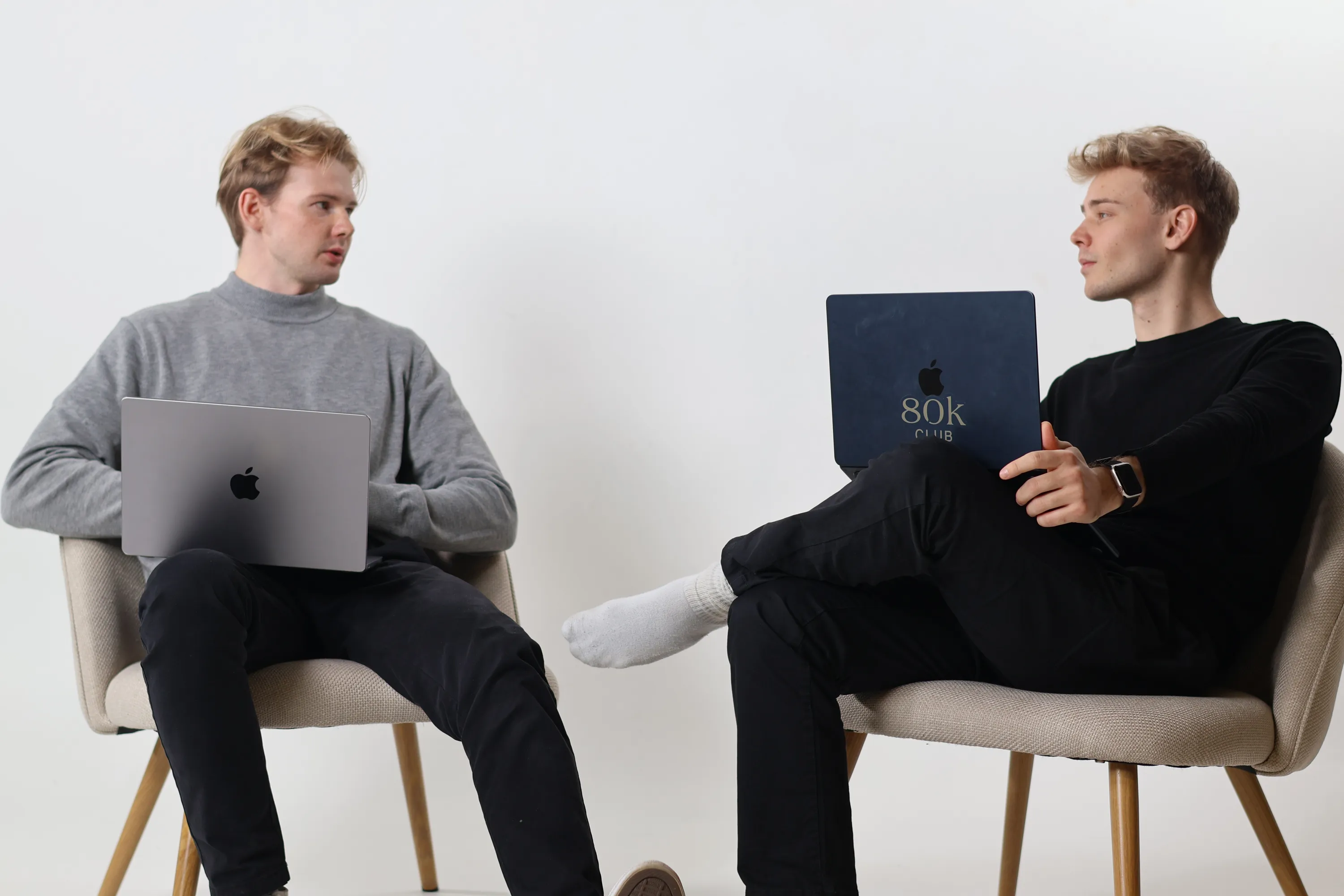 Kaksi nuorta miestä istuu tuoleilla kannettavat tietokoneet sylissään vastakkain keskustellen.