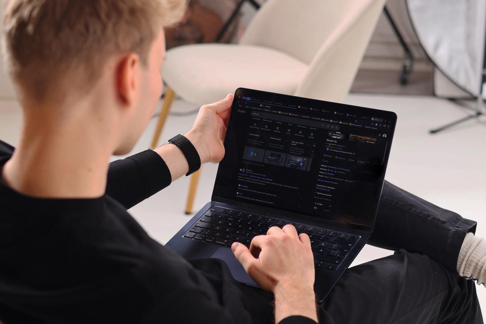Nuori mies istuu rennosti valkoisen tuolin edessä ja selaa kannettavaa tietokonettaan.