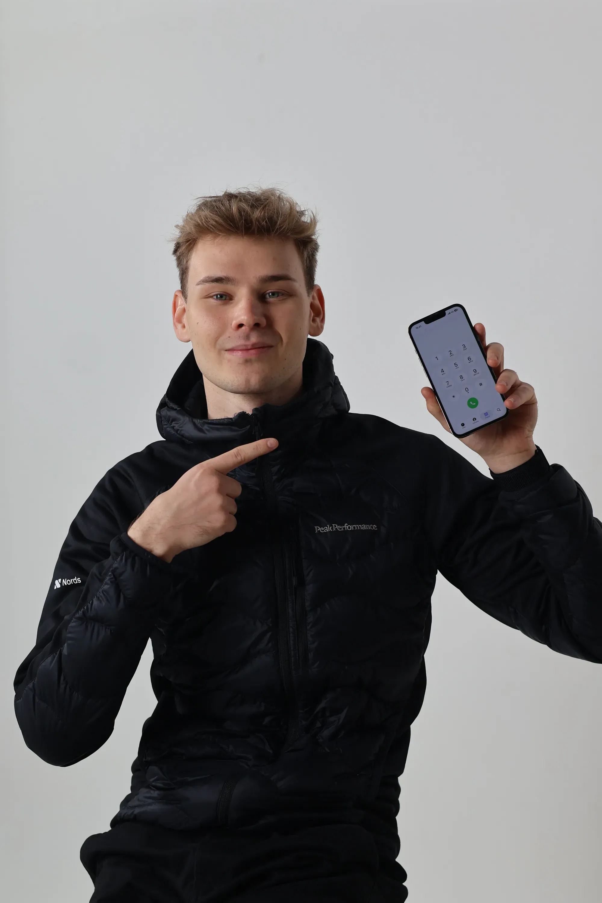 Nuori mies mustassa takissa osoittaa puhelimen näytöllä olevaa numeronvalitsinta.