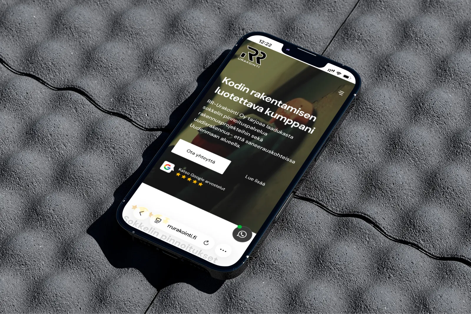 Harmaa kannettava tietokone betonijalustalla, näytöllä rakennusyrityksen verkkosivusto. Kirkas valaistus korostaa yksityiskohtia.