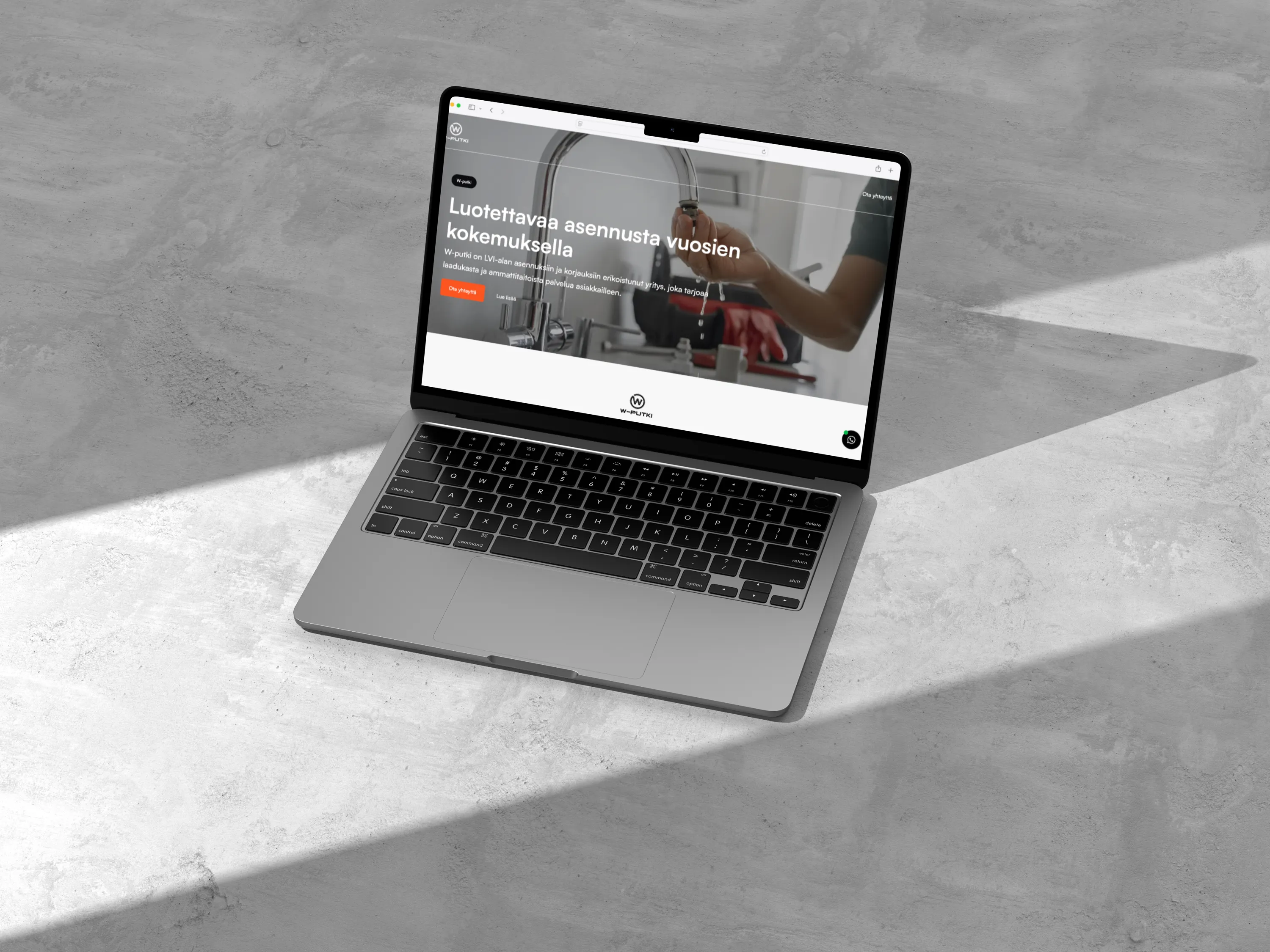 Harmaa kannettava tietokone, jossa näkyy W-putki-nimisen yrityksen verkkosivusto, valaistuna luonnonvalolla harmaalla taustalla.