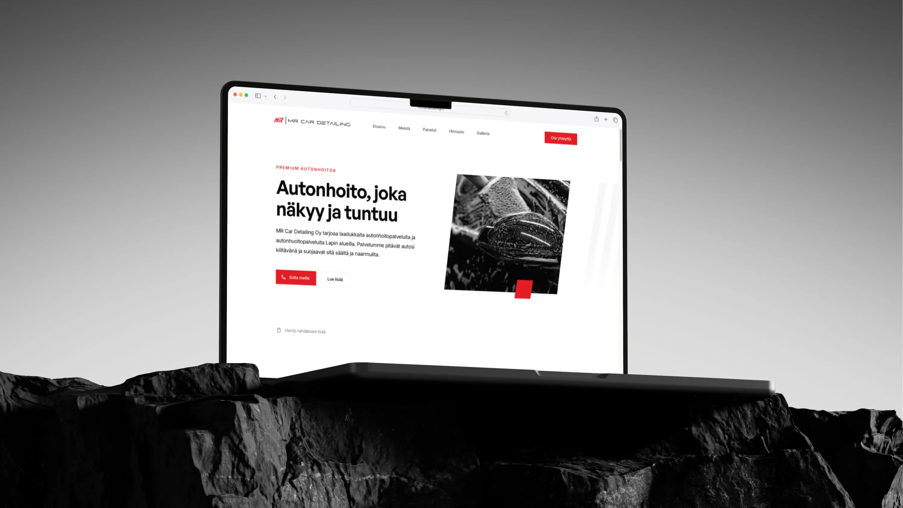 Kuva esittää kannettavaa tietokonetta, jonka näytöllä on MR Car Detailing -yrityksen verkkosivusto. Tietokone on asetettu karkealle, tummalle kivipinnalle. Sivustolla on tekstiä suomeksi, kuten "Autonhoito, joka näkyy ja tuntuu", ja punaisia painikkeita.