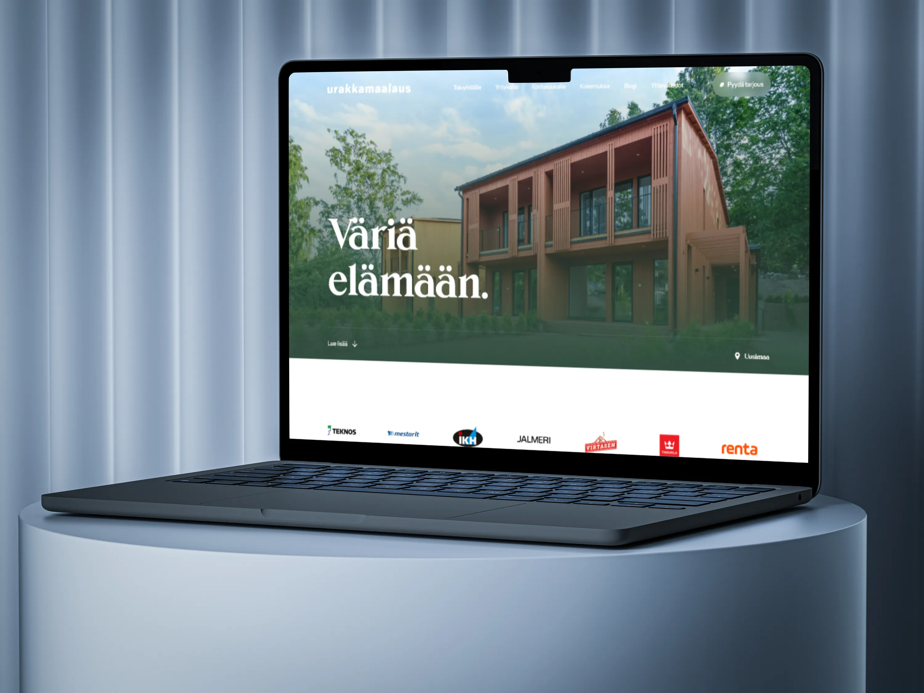Kannettava tietokone valkoisella jalustalla näyttää Urakkamaalaus-nimisen verkkosivun, jossa on tekstiä ja kuvia talosta. Sivustolla on myös useita yritysten logoja. Taustalla on sinertävä verho.