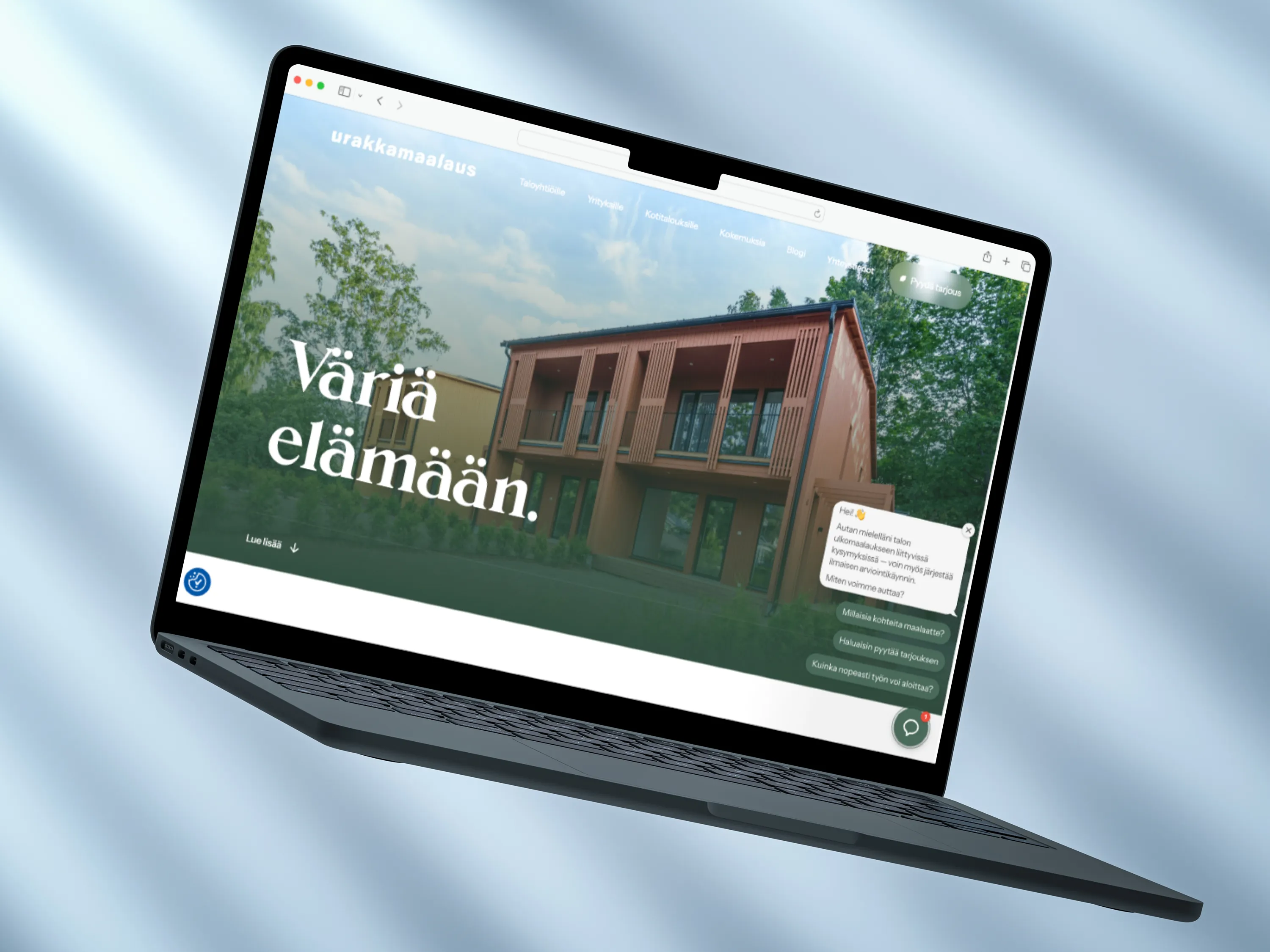 Kannettava tietokone valkoisella jalustalla näyttää Urakkamaalaus-nimisen verkkosivun, jossa on tekstiä ja kuvia talosta. Sivustolla on myös useita yritysten logoja. Taustalla on sinertävä verho.