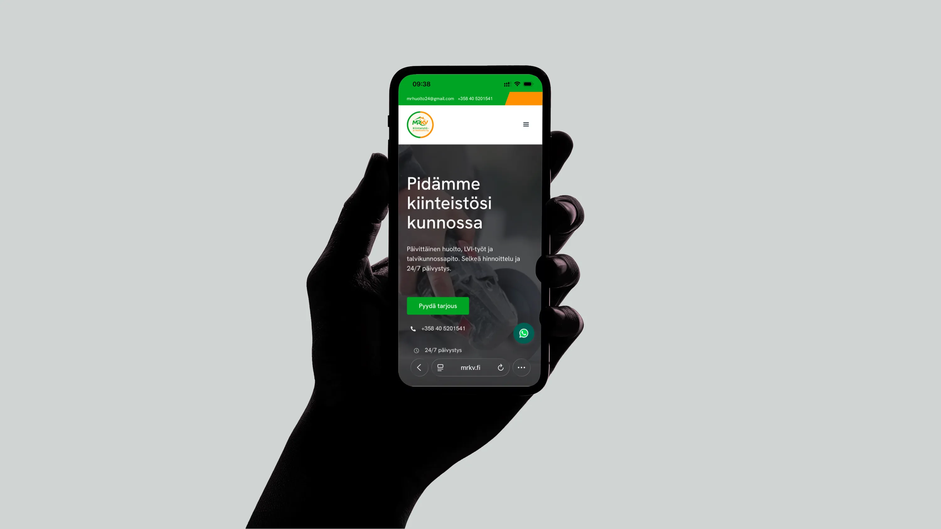Musta käsi pitelee älypuhelinta, jossa näkyy MRKV Kiinteistö -yrityksen verkkosivusto vihreällä ja valkoisella värimaailmalla.